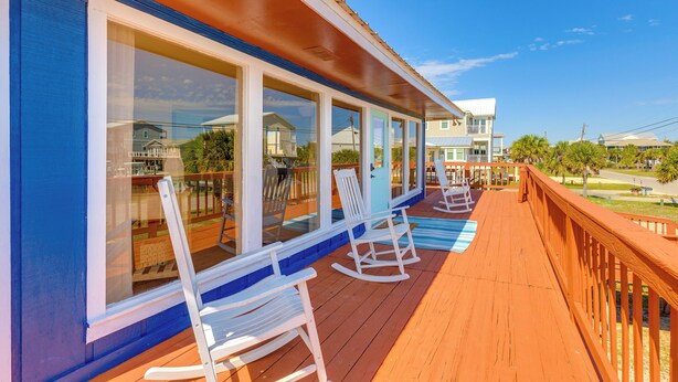 A wooden deck with white rocking chairs and large windows overlooking a residential area. - Breezy Dauphin Island Vacation Rental With Deck! (Dauphin Island)