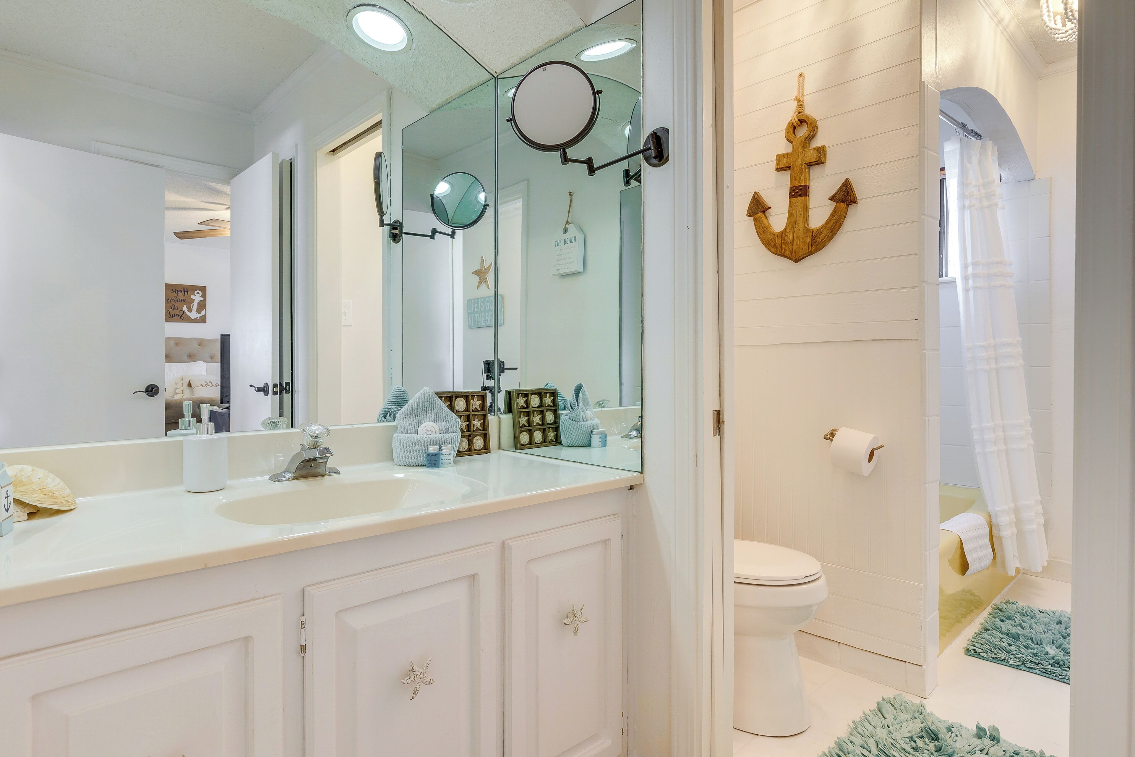 Un baño con tocador blanco, un espejo grande y una decoración de ancla de madera.