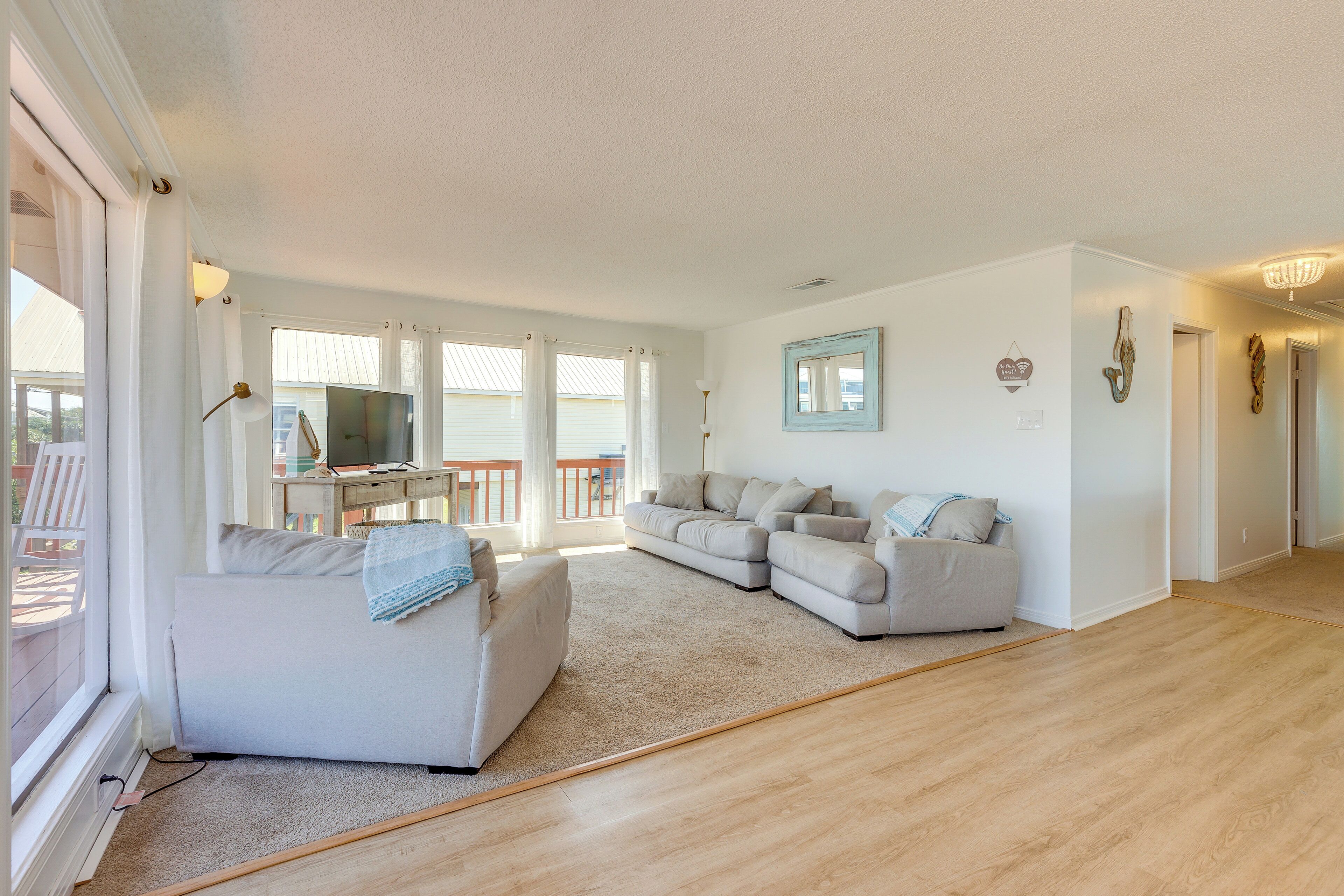 A spacious living room with a large window, a grey sofa, a smaller sofa, and a TV on a stand.