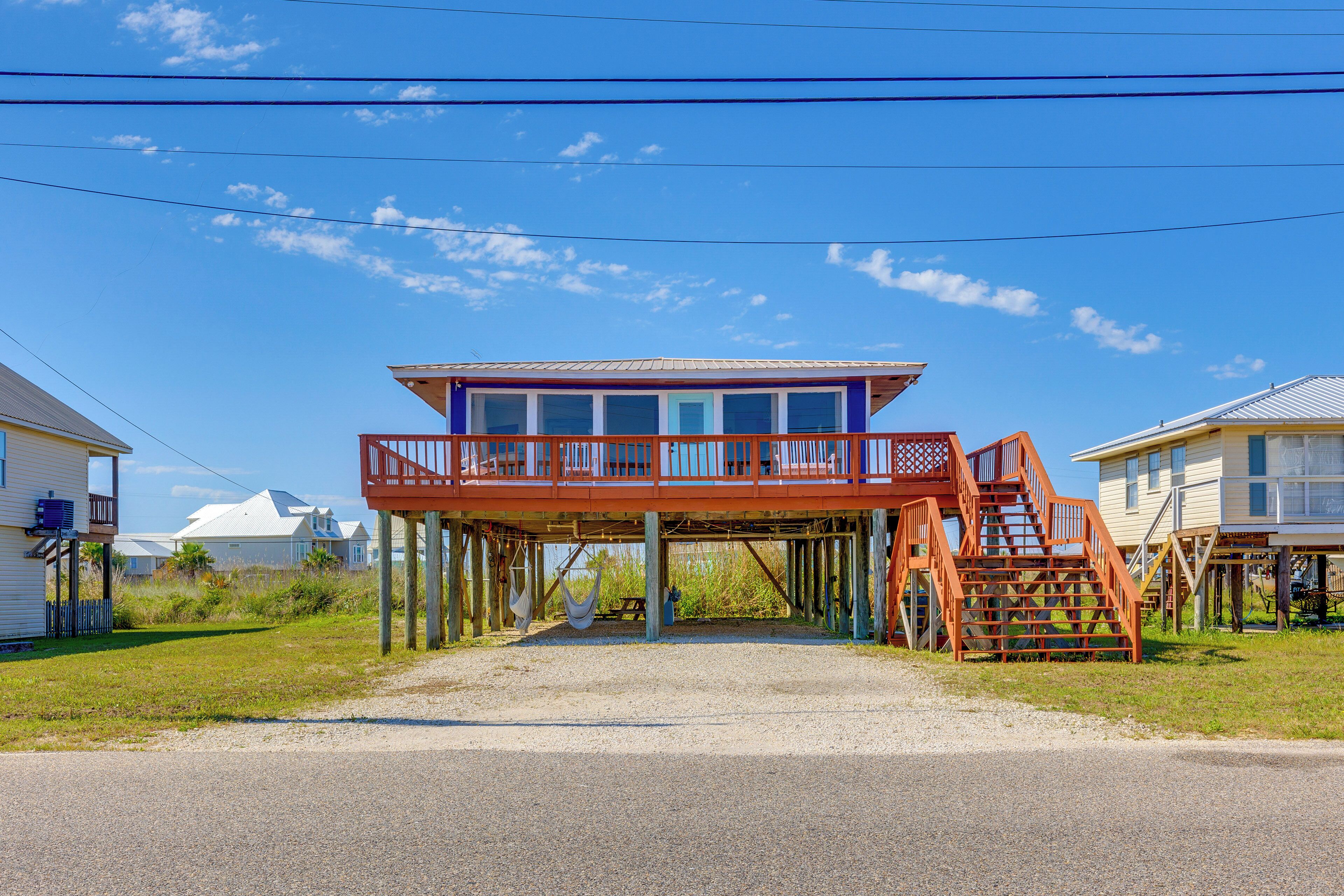 A beachfront house with a red balcony and wooden stairs leading to a covered deck.