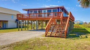 A two-story house with a wooden deck and a staircase leading to the upper floor. - Breezy Dauphin Island Vacation Rental With Deck! (Dauphin Island)