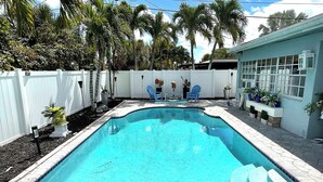 Une piscine dotée d’une terrasse blanche, entourée de palmiers et délimitée par une clôture blanche.