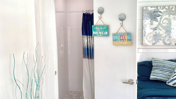 Une chambre à coucher comprenant un lit, une porte donnant sur une salle de bain et un mur orné d’objets décoratifs.