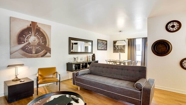 A modern living room with a grey sofa, a round coffee table, a leather armchair, a black side table, and a large wall clock. - Contemporary Dallas Condo w/ Pool Access! (Dallas)