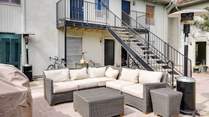 A covered outdoor seating area with a sectional sofa and ottomans, a staircase leading to an upper level, and a trash can. - Contemporary Dallas Condo w/ Pool Access! (Dallas)