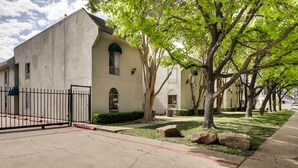 A building with a beige facade, a black metal gate, and a sidewalk with a red line. - Contemporary Dallas Condo w/ Pool Access! (Dallas)