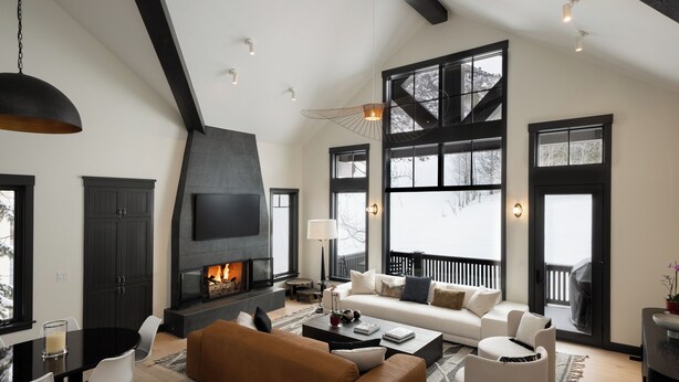 Moderni olohuone, jossa on takka, suuret ikkunat ja viihtyisä oleskelualue.