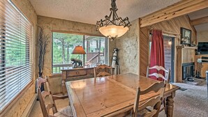 A wooden dining table with chairs, a chandelier, and a view of the outdoors through large windows. - Cozy Ruidoso Cabin w/ Private Hot Tub & Large Deck (Ruidoso)