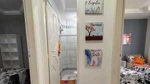 Habitación de hotel con baño, cama con colcha estampada, una mesita y un muro con tres cuadros enmarcados.