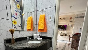 Un baño moderno con un lavabo de granito negro, baldosas de mármol blanco y un mueble de tocador blanco. Hay dos toallas colgadas en la pared y un jarrón con flores sobre la encimera.