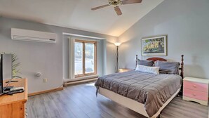 Ein Schlafzimmer mit Bett, Deckenventilator, Klimaanlage, Nachttisch, Lampe, einem Gemälde und einem Fenster.
