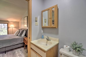 A bedroom with a bed, bedside table, and a bathroom with a sink, mirror, and toilet. - Poconos Retreat w/ Pool & Deck, Near Lake Harmony! (Lake Harmony)