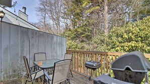 Eine Holzterrasse mit Tisch, Stühlen, einem Grill und einem Holzzaun.