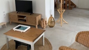 Uma sala de estar com televisão, móveis de madeira, uma poltrona de vime e uma escada.