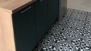 Uma cozinha moderna com bancada de madeira, armários pretos e piso de azulejos estampados.