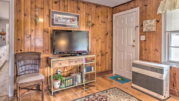 Een woonkamer met houten lambrisering, een televisie op een houten dressoir, een boekenkast, een stoel en een airconditioner.