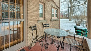 Eine überdachte Terrasse mit Backsteinwand, Glastür und einem Metalltisch mit Stühlen.