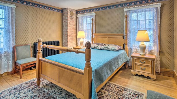 Ein traditionelles Schlafzimmer mit einem hölzernen Himmelbett, zwei Nachttischen mit Lampen, einem Sessel und gemusterten Teppichen.
