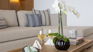 A modern living room with a sofa, pillows, a coffee table, a vase with white orchids, two glasses of white wine, and a bowl of decorative eggs.