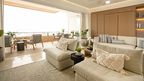 A spacious living room with a large window, a ceiling fan, and a view of the ocean.