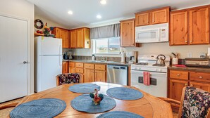 A kitchen with wooden cabinets, a refrigerator, a microwave, a dishwasher, and a dining table with placemats. - Ranch House in Boulder! Gateway to Nearby Parks! (Boulder)