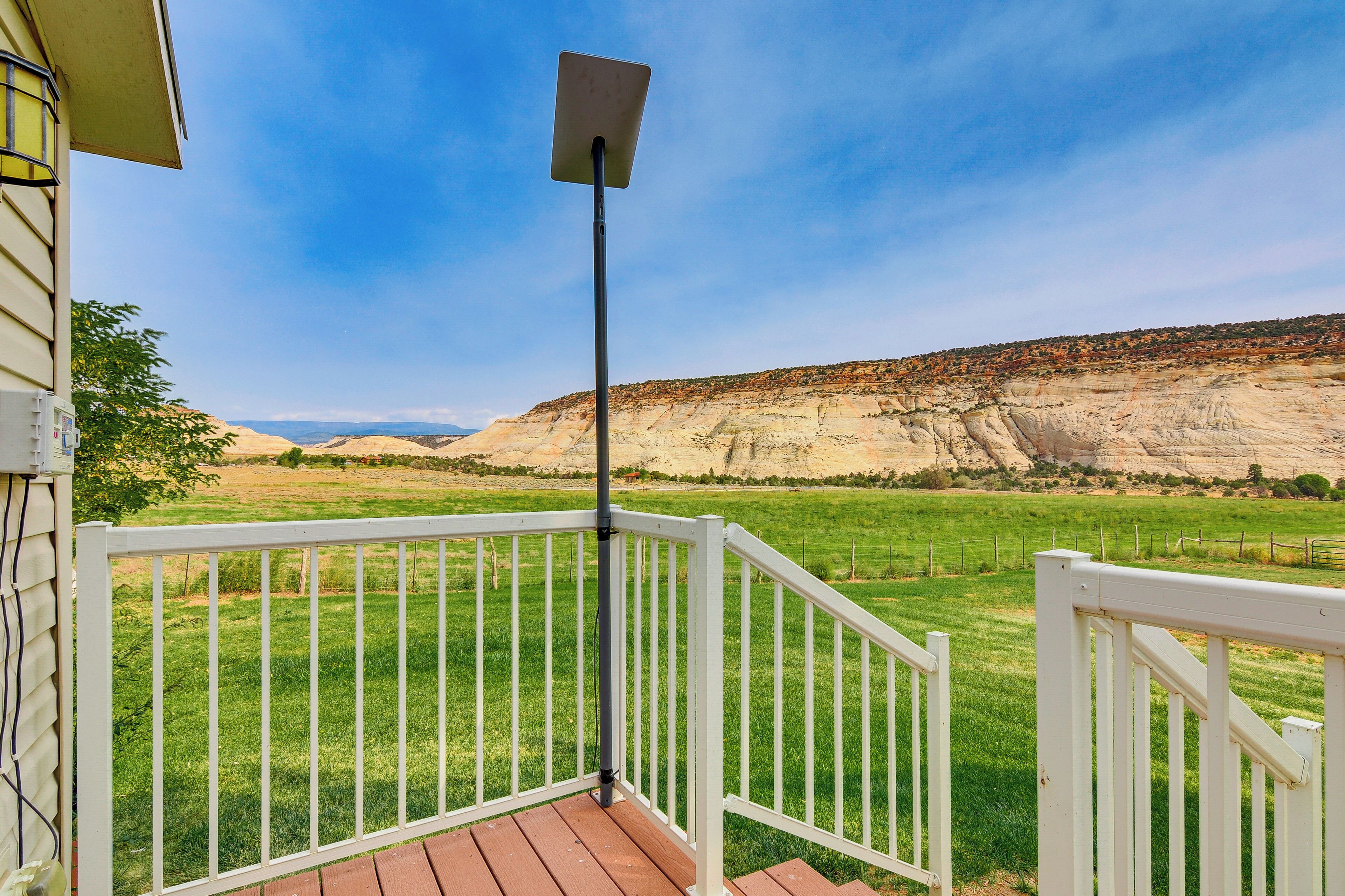 A deck with a white railing overlooking a green field and a rocky hillside.