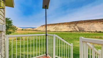 A deck with a white railing overlooking a green field and a rocky hillside.