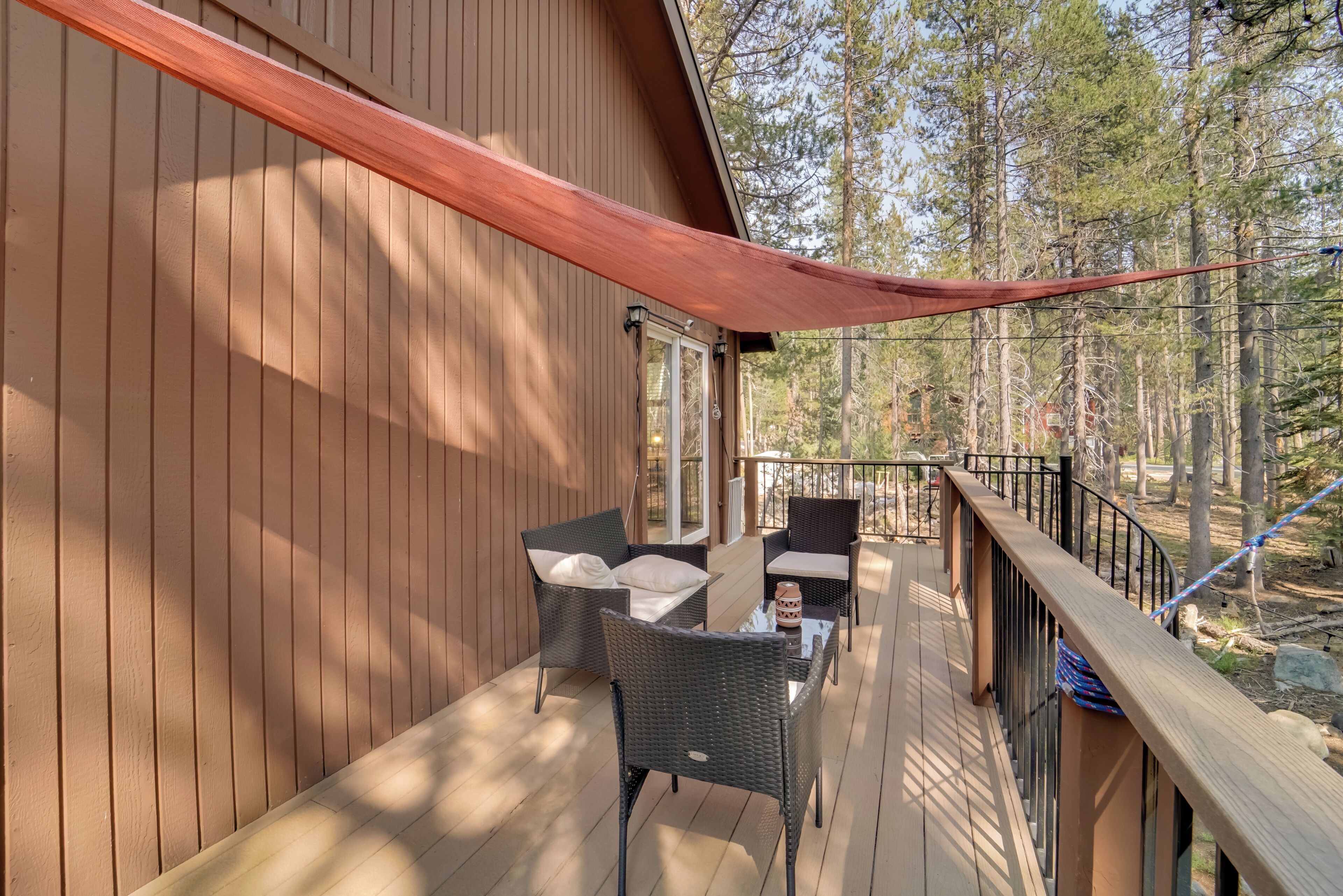 Una terraza de madera con mobiliario de mimbre y un toldo rojo.