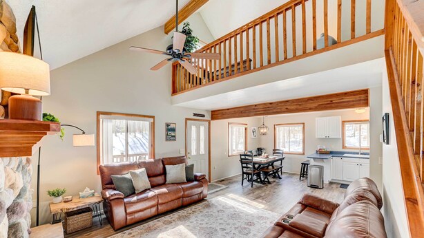 A spacious living area with a brown leather sofa, a dining table, and a kitchen in the background. - Roscommon Retreat w/ Deck ~ 1 Mile to Higgins Lake (Roscommon)