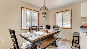 A dining area with a wooden table, chairs, and a bench. There are two windows with wooden frames, a hanging light fixture, and a sign on the wall. - Roscommon Retreat w/ Deck ~ 1 Mile to Higgins Lake (Roscommon)
