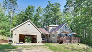 A two-story house with a garage, a covered porch, and a wooden deck. - Roscommon Retreat w/ Deck ~ 1 Mile to Higgins Lake (Roscommon)