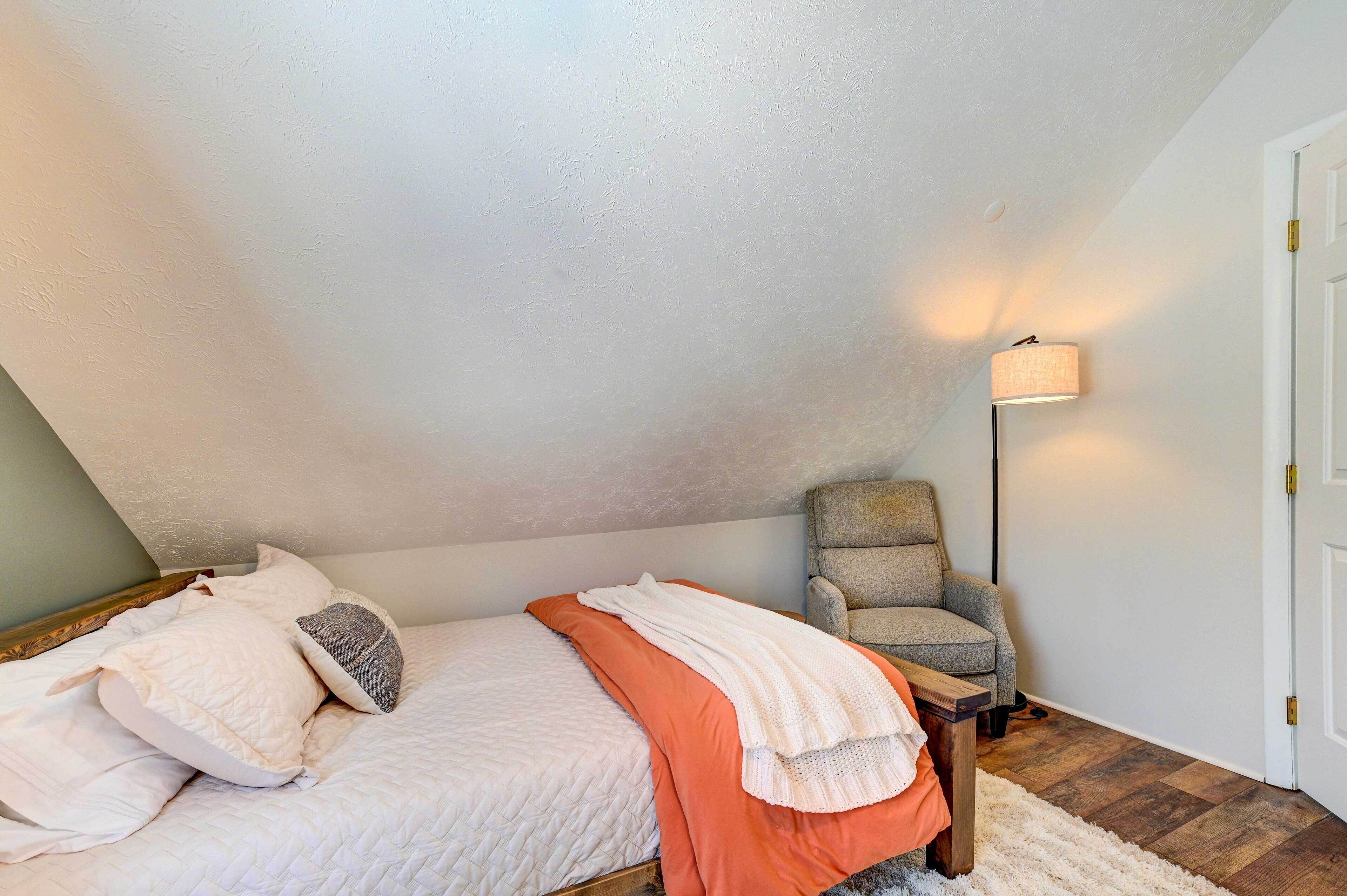 Ein Schlafzimmer mit Bett, Kissen, einem Sessel, einer Lampe und einer Tür.