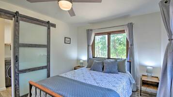 A bedroom with a bed, a ceiling fan, a window with curtains, and a nightstand with a lamp.