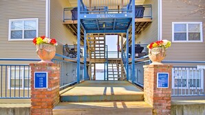 A building entrance with a blue staircase leading up to a balcony. There are two flower pots with flowers on either side of the entrance.