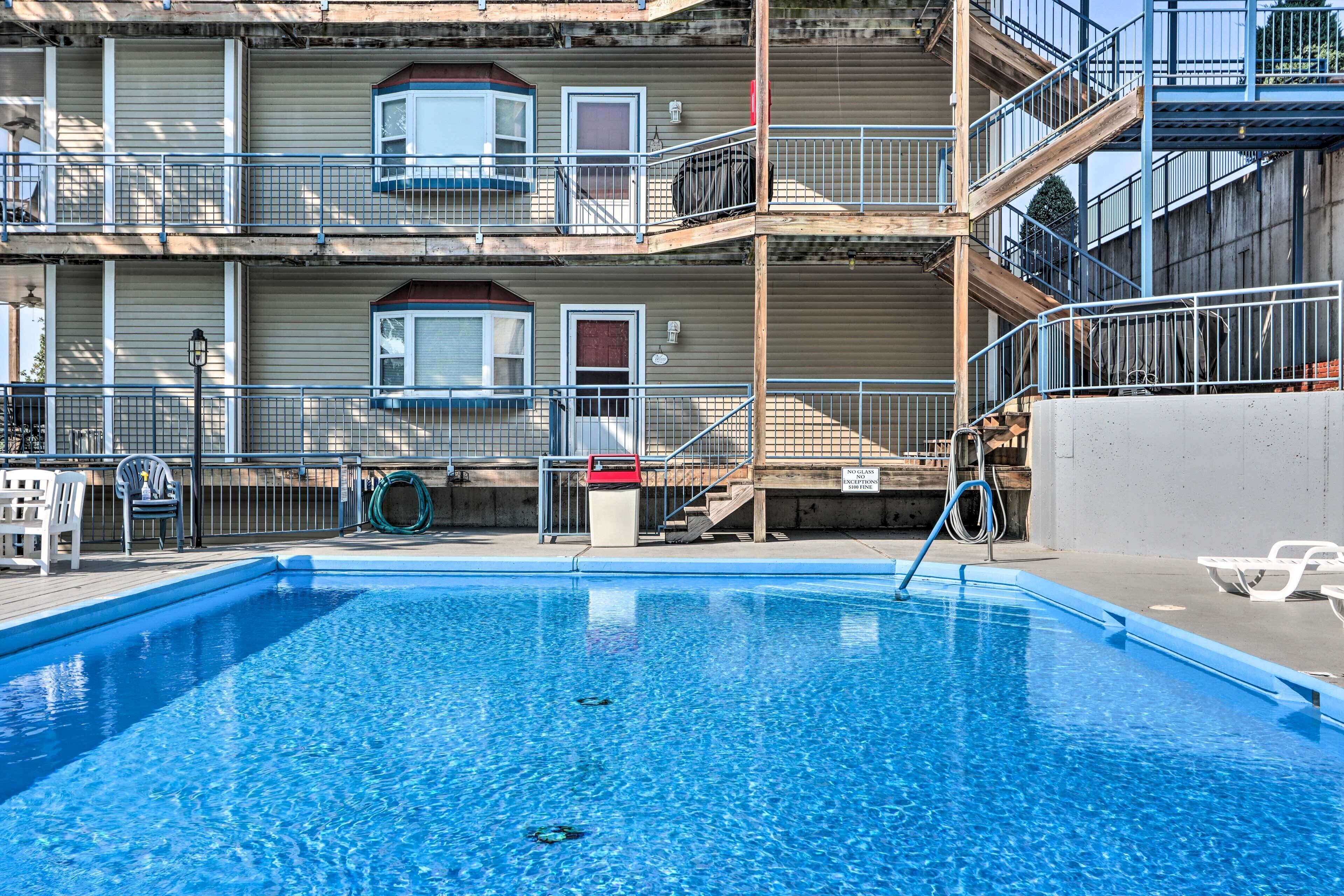 A swimming pool with a wooden deck, a red car, and a multi-story building with balconies and railings.