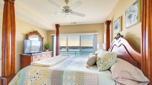 A bedroom with a large bed, a ceiling fan, a TV, and a view of the ocean.