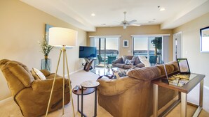 A spacious living room with a sofa, a coffee table, and a TV. There is a balcony with a view.