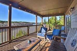 Une terrasse couverte, aménagée avec des meubles en osier et une table en verre, qui offre une vue sur une rivière et une forêt.