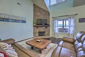 A living room with a stone fireplace, leather sofas, a flat-screen TV, and a painting of sailboats.