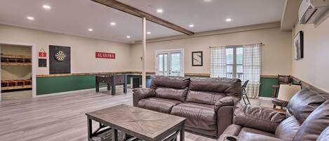 A spacious living area with a leather sofa, a wooden coffee table, and a dartboard.