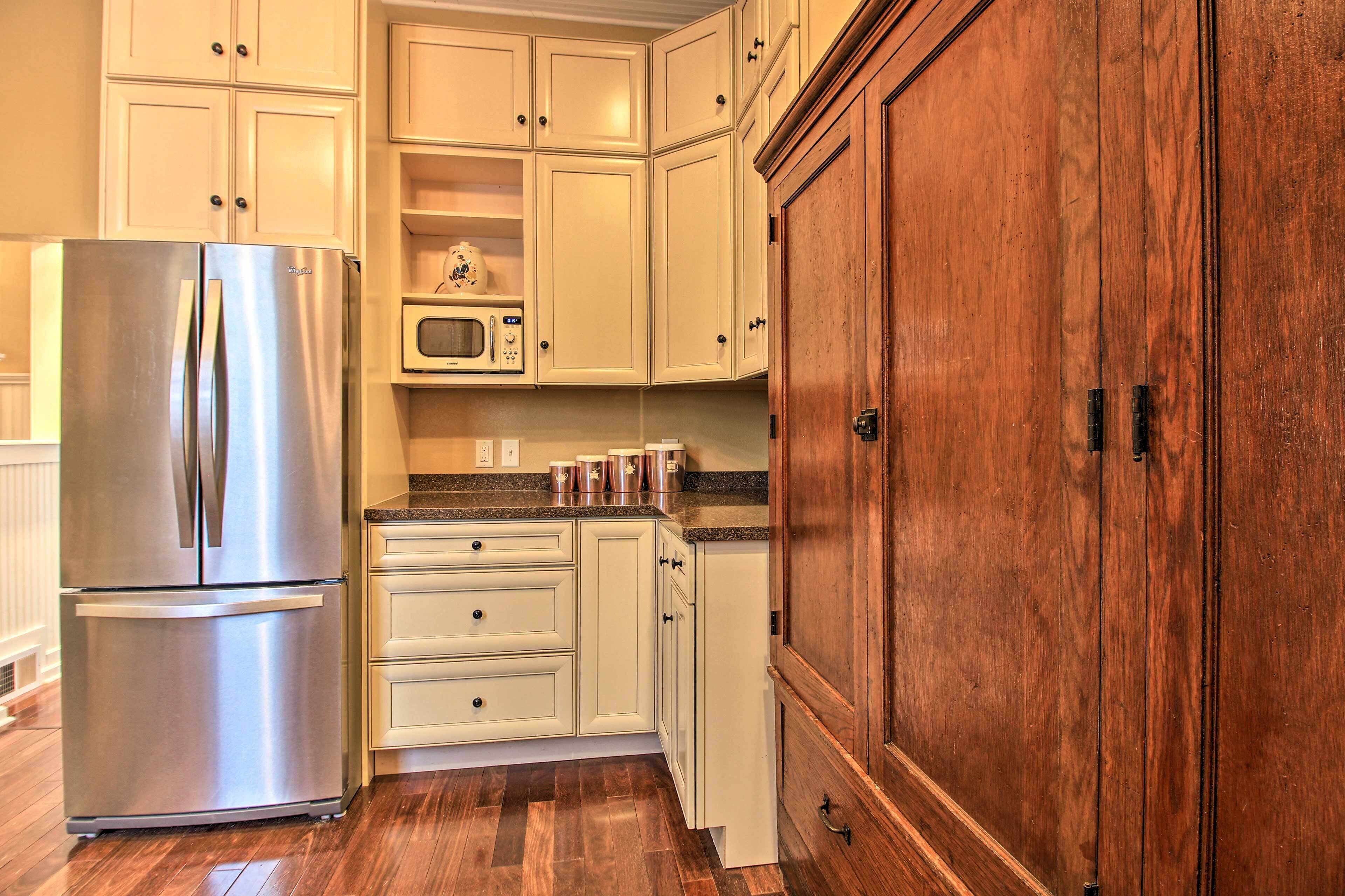 A kitchen with white cabinets, a stainless steel refrigerator, a microwave, and wooden cabinets.