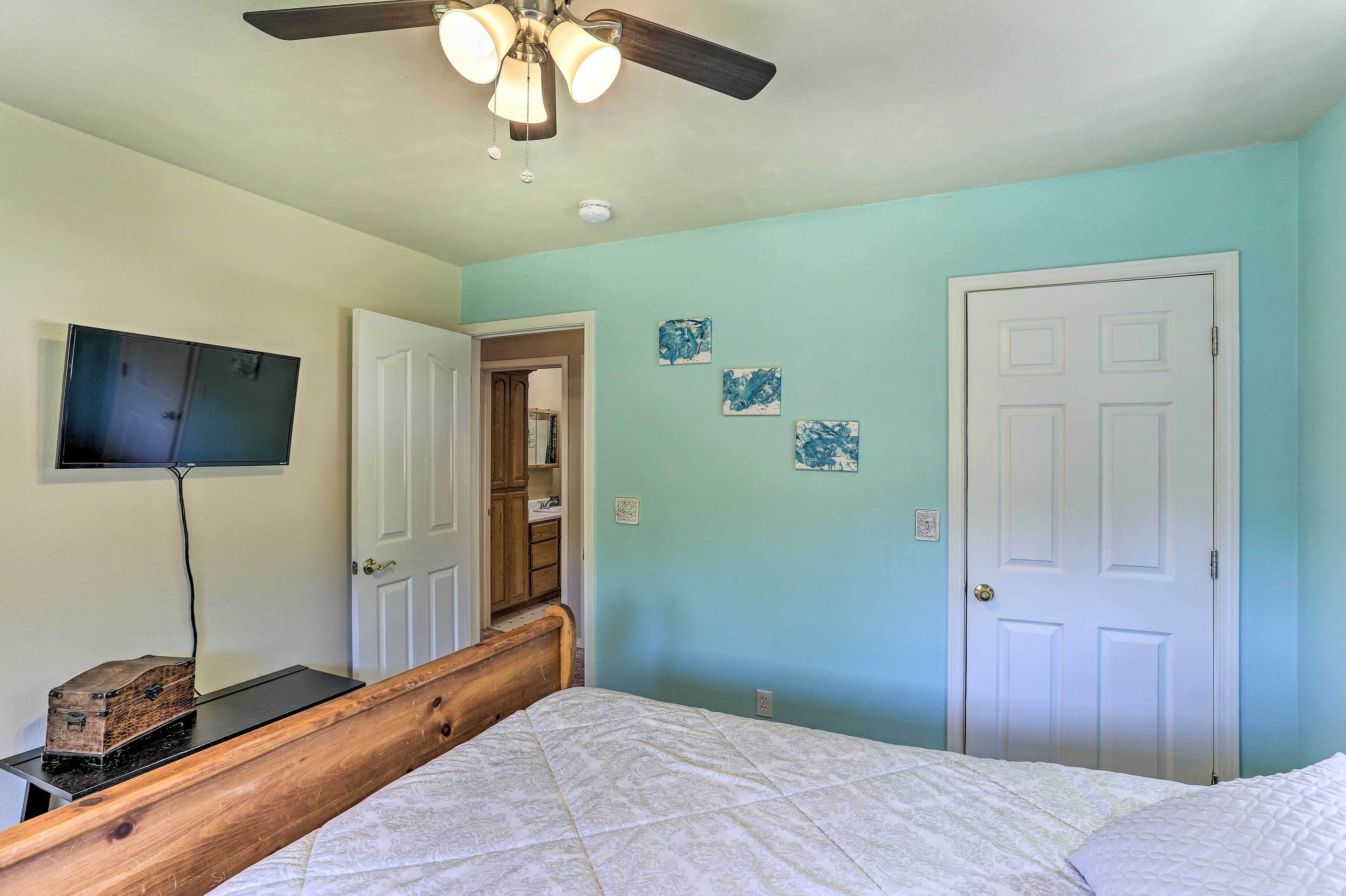 A bedroom with a bed, a ceiling fan, a television, and a door.