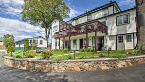 A two-story house with a balcony, stone retaining wall, and a large tree in front. - Homey Laconia Home w/ Private Porch & Grill (Laconia)
