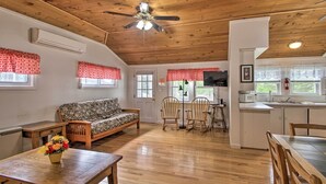 A cozy interior with a wooden ceiling, a sofa, a dining table, and a kitchen area. - Homey Laconia Home w/ Private Porch & Grill (Laconia)