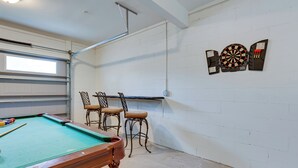 Ein Billardtisch mit vier Stühlen, eine Dartscheibe und ein Fenster in einem Raum mit weißen Backsteinwänden.