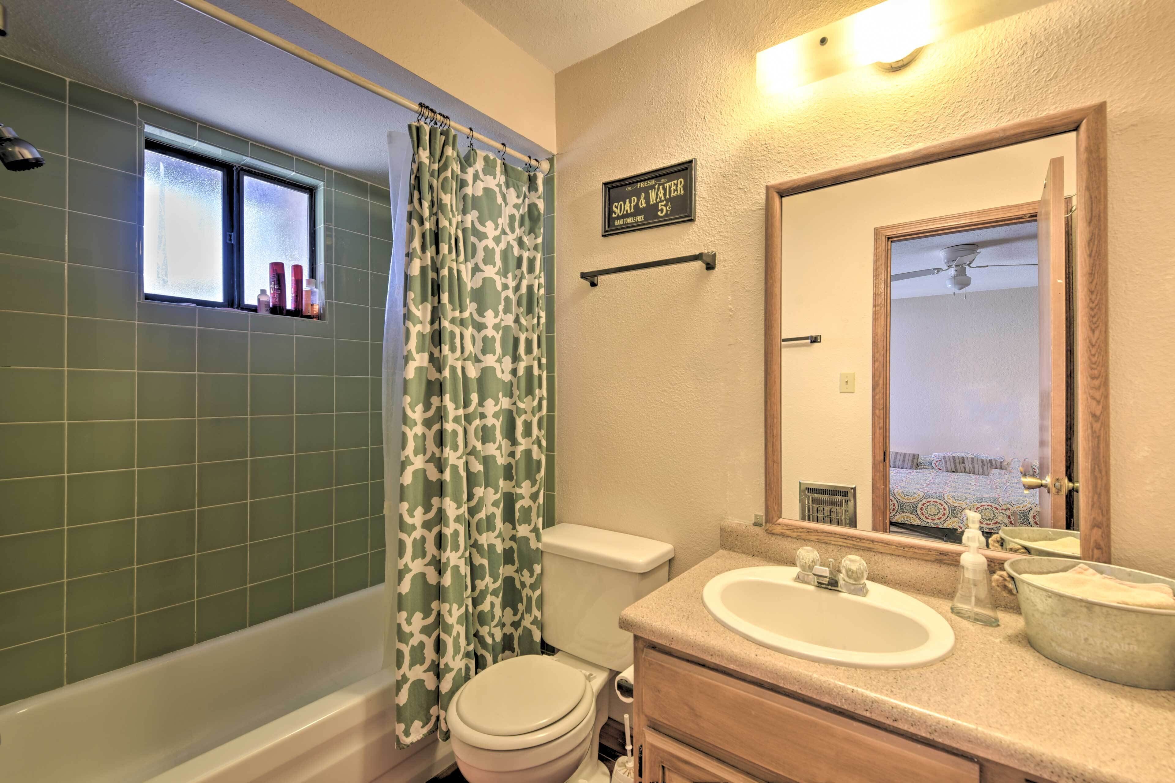 Une salle de bain avec une baignoire, des toilettes et un lavabo. Il y a un rideau de douche et une fenêtre au-dessus des toilettes.