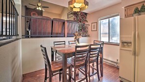 A dining area with a wooden table and chairs, a hanging light fixture, a clock on the wall, and a window with a view. - Quaint Angel Fire Townhome: 1/2 Mi to Ski Slopes! (Angel Fire)