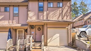 A two-story building with a garage door, a front porch with steps, and a small outdoor area with a blue umbrella. - Quaint Angel Fire Townhome: 1/2 Mi to Ski Slopes! (Angel Fire)