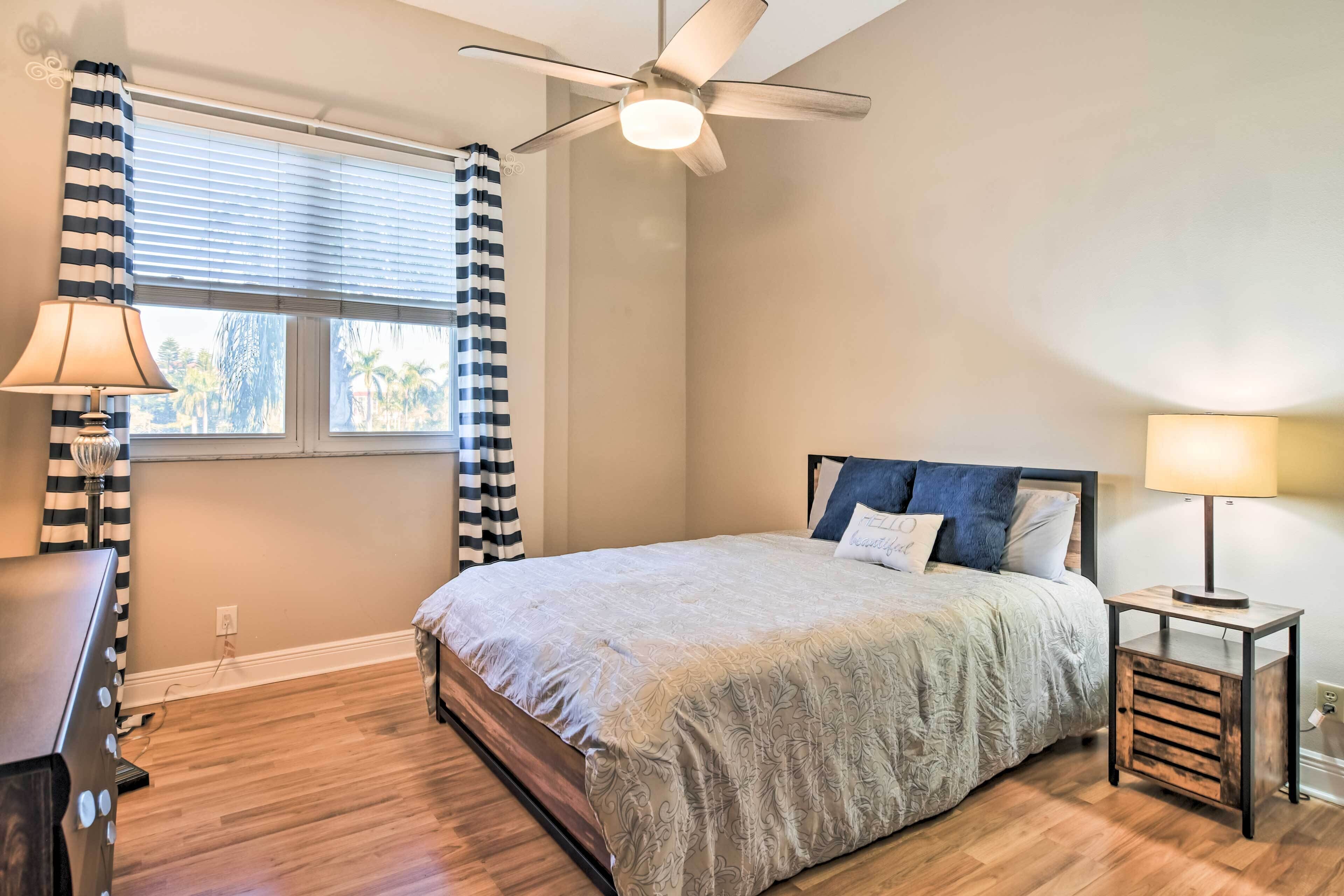 A bedroom with a bed, a ceiling fan, a window with curtains, a nightstand, and a lamp.