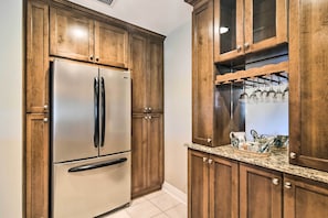 A kitchen with wooden cabinets, a stainless steel refrigerator, a granite countertop, and a wine rack. - St Pete Condo w/ Private Lanai & Community Pool! (St. Petersburg)